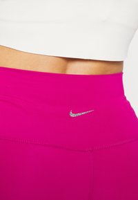 Fuchsiové legíny s vysokým pasem vyrobené z elastického materiálu, se stříbrným logem Nike na pasu a plochými švy pro pohodlí.