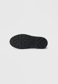 Schwarze Gummisohle mit strukturiertem Profil und Mustern für besseren Halt, flache Ferse und eine abgerundete Zehenpartie mit minimalen Details.