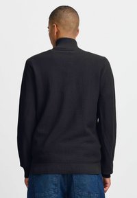 Schwarzer, strukturierter Reißverschluss-Pullover mit hohem Kragen und gerippten Bündchen, der ein minimalistisches Design und einen lässigen Schnitt aufweist.