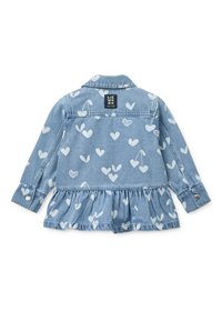 Τζιν μπουφάν με ανοιχτό μπλε ύφασμα, διακοσμημένο με λευκά μοτίβα καρδιάς και κερασιών, με βολάν στο τελείωμα και κουμπωτά μανίκια. Φέρει την ετικέτα «LIEWOOD».