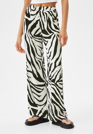 Kvinde iført sort-hvide zebramønstrede bukser med brede ben og elastisk talje samt sorte plateauflip-flops, beskåret ved maven.