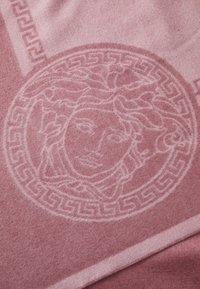 Pătură tricotată roz cu un design Medusa și un model cu chei grecești, având o textură moale și nuanțe contrastante în țesătură.