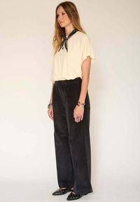 Chemise jaune à manches courtes, pantalon large en velours côtelé noir, ballerines noires pointues et une écharpe noire à motif nouée autour du cou.