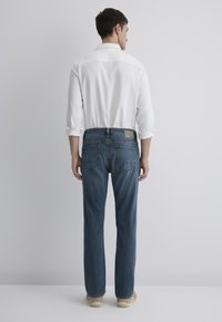Men's light blue jeans with a straight-leg fit, featuring a classic five-pocket design and a plain back with a patch label. Worn with a white shirt.