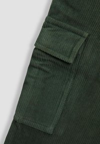 Sötétzöld kordbársony anyag függőleges bordákkal. Jellemzője egy fedéllel ellátott zsebpocket, látható varrás, és sima tapintás.