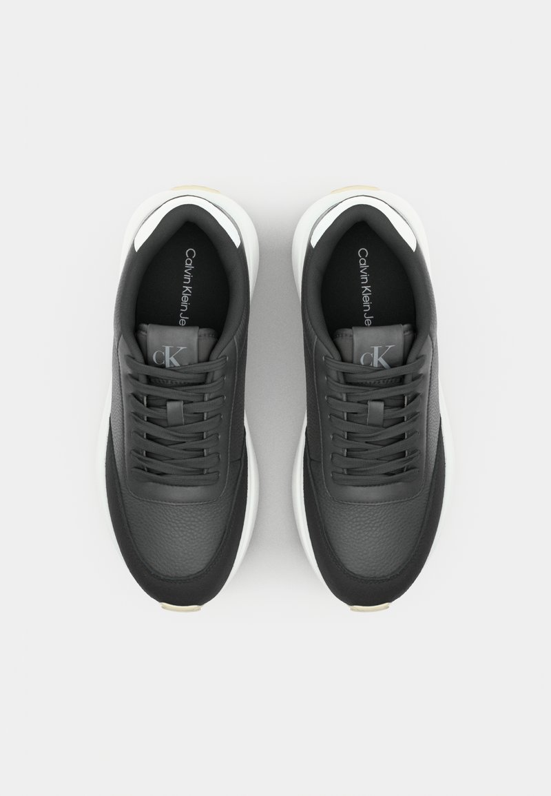 Zwarte leren sneakers met een gestructureerde afwerking, witte zolen, platte veters en een logo-label. Voorzien van subtiele accentdetails in het wit bij de hiel.