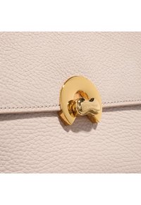 Sac à main en cuir beige clair avec fermeture à clapet ronde en ton or et surface lisse avec un léger grain.