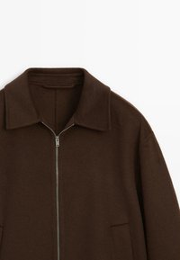 Brun, lynlåsjakke med en bred krave, sidelommer og et blødt, struktureret stof. Rent design uden synlige mønstre eller accenter.