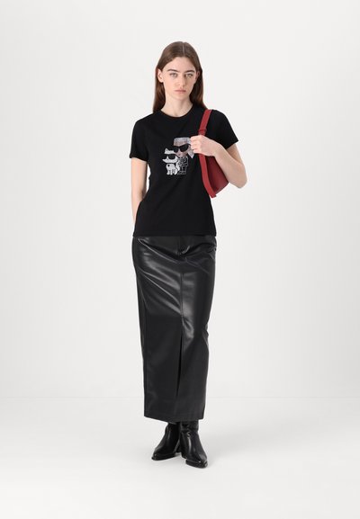 T-shirt noir avec un graphique de dessin animé, associé à une longue jupe en cuir noir et des bottines noires, complété par un sac à bandoulière rouge.