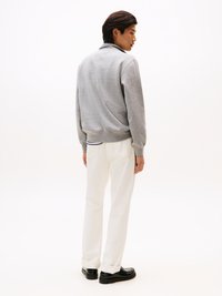 Sweatshirt gris avec col, coupe décontractée et poignets côtelés, associé à un jean blanc retroussé et des chaussures noires. Fond neutre.