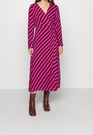 Langærmet slå-om-kjole i levende pink og lilla striber. Har en V-udskæring og et bindebånd ved taljen, kombineret med brune støvler med hæl.