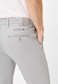 Pantaloni grigi in tessuto strutturato, dotati di tasche, chiusura con bottone e un'etichetta con logo sul retro della vita.