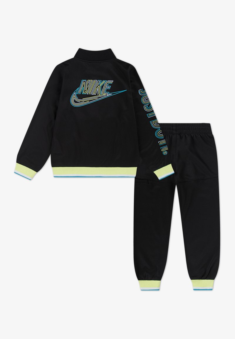 Conjunto de chaqueta y pantalones deportivos negros con un acento en amarillo neón, logotipos azules y verdes, puños acanalados y cinturilla elástica.