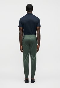 Μπλε ναυτικό T-shirt με κοντά μανίκια, συνδυασμένο με πράσινο παντελόνι σε στενή γραμμή με ελαστική μέση και τελειώματα με λάστιχο. Μαύρα παπούτσια συμπληρώνουν την εμφάνιση.