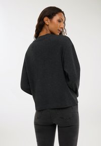 Czarny sweter w ciemnoszarym kolorze o luźnym kroju, z prążkowanym dekoltem i opadającymi ramionami, w zestawieniu z czarnymi dżinsami. Miękka faktura, minimalne detale.