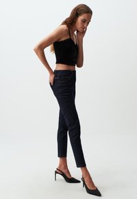 Top corto in velluto nero con spalline sottili abbinato a jeans a vita alta blu scuro e scarpe con tacco a rocchetto nere.