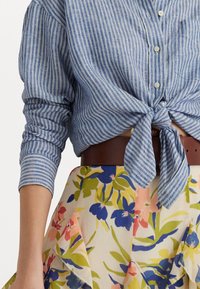 Sininen ja valkoinen raitapaita, joka on solmittu vyötärölle, yhdistettynä kukkakuosisesti hameeseen, jossa on röyhelöitä. Ruskea vyö korostaa vyötäröä.