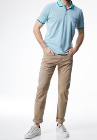 Sininen raidallinen polo-paita, jossa on kaulus ja nappiyksityiskohtia, yhdistettynä beigeihin käännettyihin chinopantsiin ja valkoisiin tennareihin. Yksinkertainen, rento istuvuus.