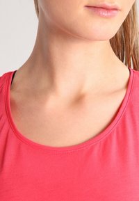 Top rosa a maniche corte e collo rotondo, realizzato in tessuto morbido; presenta una texture liscia e cuciture minime nel collo.