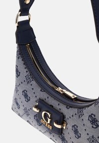 Navy patterned shoulder bag with a gold logo, featuring a zip closure and smooth textured straps. Material is denim-like with accents.