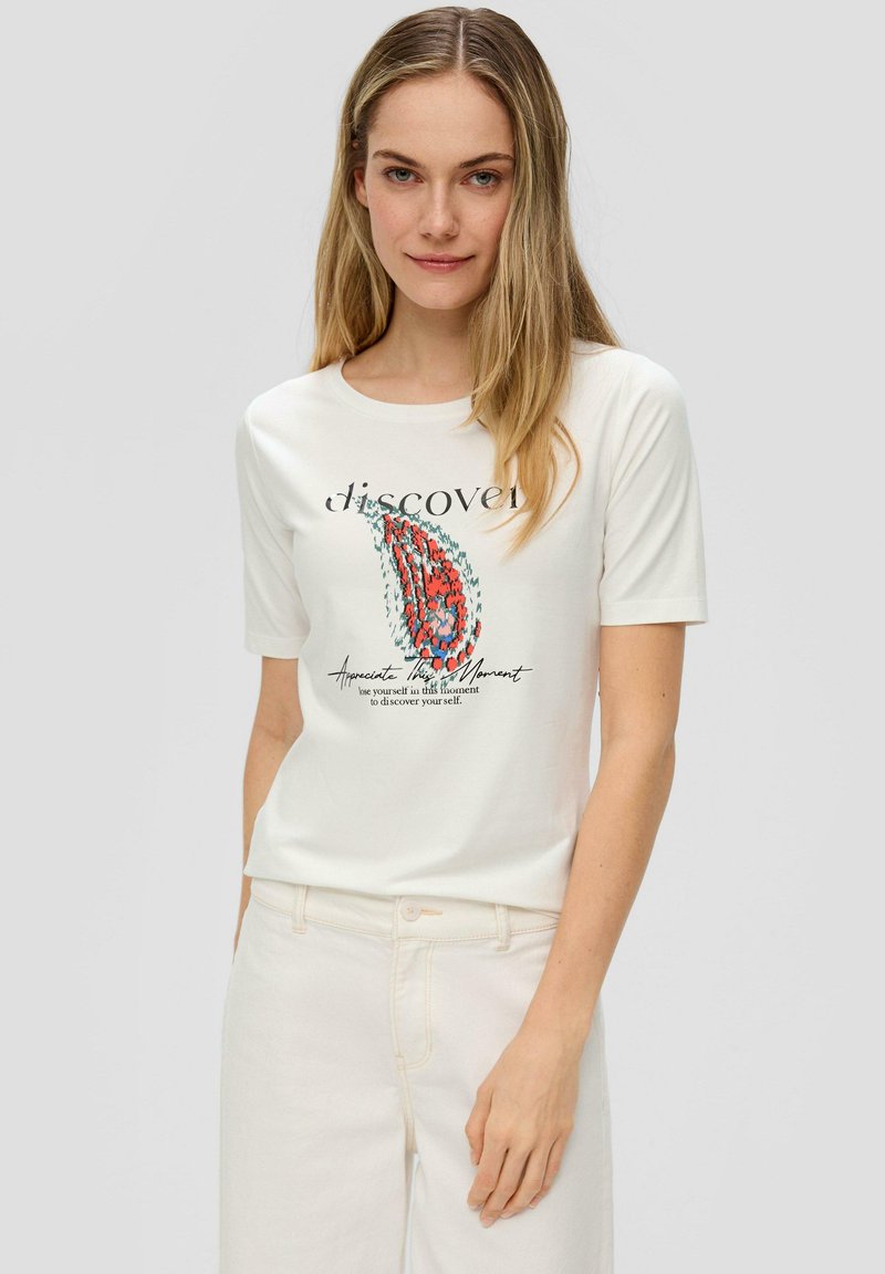 T-shirt blanc à manches courtes avec un design graphique coloré et du texte. Le tissu semble doux et léger. Porté avec un pantalon de couleur claire.