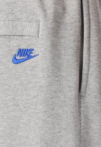Siva dukserica narejena iz mehkega materiala, z modrim vezenim Nike logotipom. Ima žep in preprost, sproščen dizajn.
