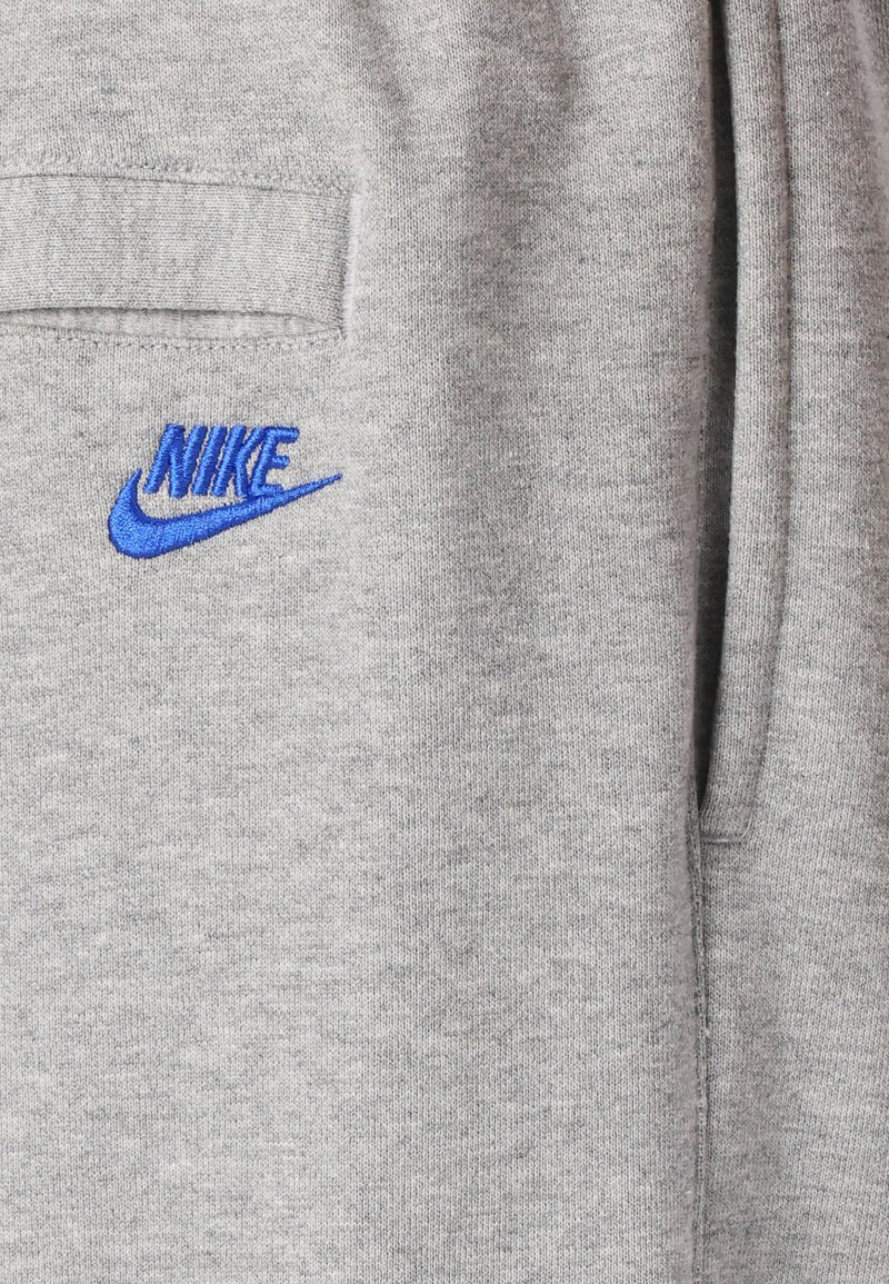 Szara bluza z miękkiego materiału, z niebieskim haftowanym logo Nike. Zawiera kieszeń i ma prosty, casualowy design.