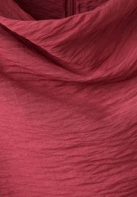 Tissu rouge avec texture de tissage visible, légères rides et un pli courbé près du centre supérieur.