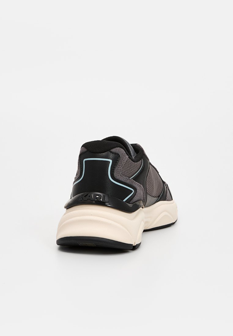 Zapatillas deportivas en negro y gris que cuentan con una parte superior de malla, un cuello acolchado y una suela gruesa de color crema con sutiles acentos azules y detalles de marca.