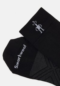 Calcetines negros de mezcla de lana, con un logo gris claro y un agarre estampado en las suelas. Textura suave con puños elásticos.