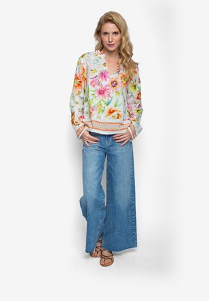 Kwiatowa bluzka w żywe wzory w kolorach różu, pomarańczu i zieleni, z dekoltem w serek i długimi rękawami; w połączeniu z szerokimi dżinsami o szerokich nogawkach.