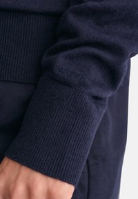 Manga de suéter de punto en color marino con puño acanalado, que presenta un discreto detalle del logo GANT. Textura suave, diseño ajustado y color uniforme.