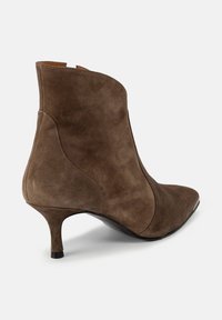 Botă ankle din suede maroniu cu vârf ascuțit și un design curbat. Dispune de un toc de 6.5 centimetri și o textură netedă, fără accente suplimentare.