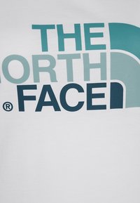 Vit bomull t-shirt med en stor logotyp i teal och marinblå som säger "THE NORTH FACE." Slät textur med minimala designelement.