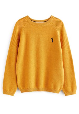 Pull en maille jaune moutarde avec épaules et poignets côtelés, avec un petit emblème de tête de cerf bleu marine sur la poitrine gauche.
