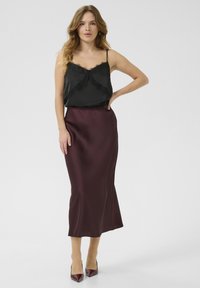 Svart satin camisole med spetsdetaljer, i kombination med en bordeaux satin maxi kjol. Modellen bär pumps med spetsig tå. Slät textur genomgående.
