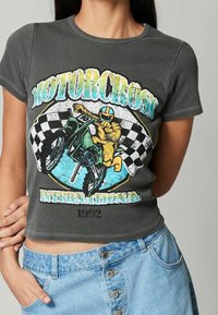 Grå cropped t-shirt med et motocross grafik, der viser en rytter på en grøn motorcykel, ternet flag og farverig tekst.