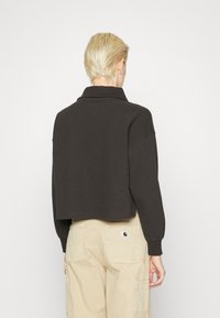 Maglione croppato di colore nero con texture a waffle e colletto, con maniche lunghe e polsini a coste, indossato sopra pantaloni cargo beige.