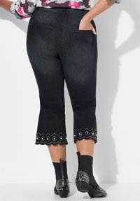 Pantalons capri en denim noir avec un ourlet festonné présentant des découpes complexes et des embellissements métalliques ; deux poches arrière.