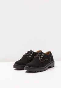 Scarpe stringate in suede nero con punta arrotondata, tacco basso e suola in gomma testurizzata; presentano cuciture a contrasto e dettagli con occhielli.