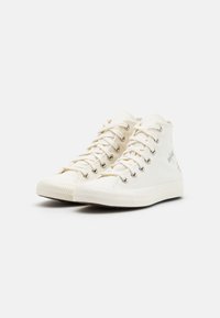 Tenisky s vysokým střihem vyrobené z off-white plátna, s kovovými očky, plochými tkaničkami a gumovou podrážkou. Na bocích jsou malé barevné grafiky.