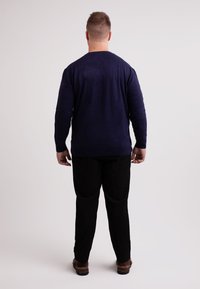 Marineblauer Pullover mit langen Ärmeln, aus weichem Stoff, kombiniert mit schwarzen Hosen. Das Outfit hat eine lockere Passform und einen runden Ausschnitt.