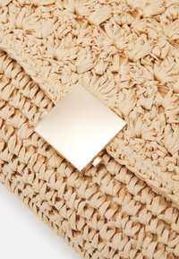 Borsa di paglia intrecciata beige con una chiusura quadrata dorata liscia e una superficie testurizzata, caratterizzata da nodi intricati e un rivestimento in tessuto naturale.