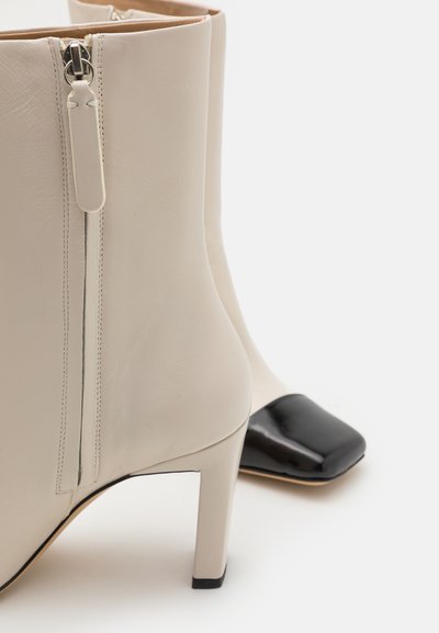 Beige leren enkellaarsjes met een gladde textuur en een zijrits, voorzien van een zwarte vierkante neus en een slanke hoge hak.