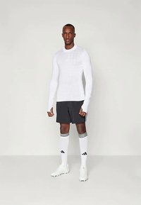 Biely dlhý rukáv s textúrovaným vzorom, čierne šortky, biele ponožky s tromi čiernymi pruhmi a biele kopačky.