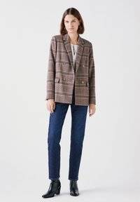 Bruin geruit double-breasted blazer met gouden knopen, gestructureerde stof, met schouderpees; gecombineerd met donkerblauwe jeans en zwarte enkellaarsjes.