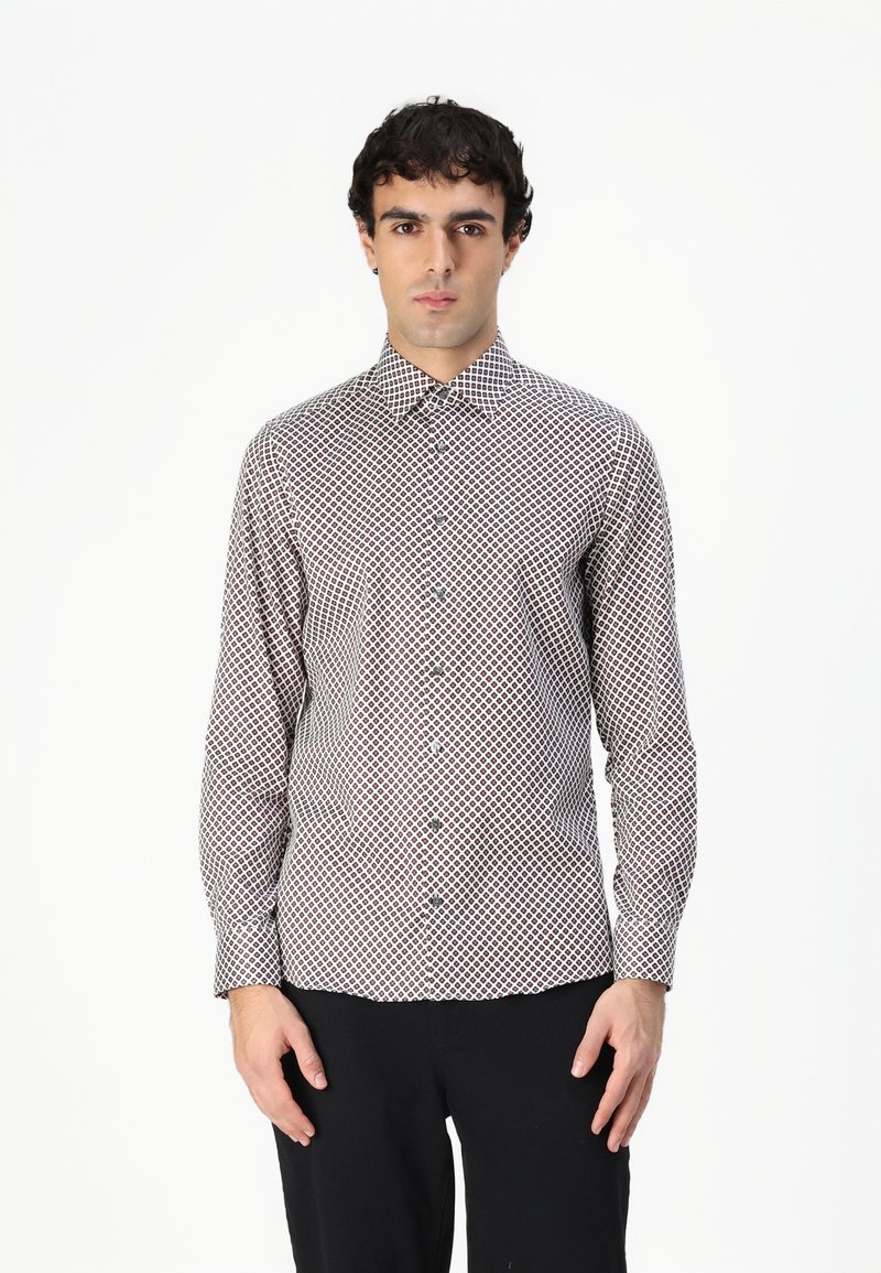 Chemise à manches longues boutonnée blanche avec un motif en losanges rouge et marine. Dispose d'un col pointu et d'une coupe ajustée.