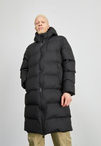 Zwarte pufferjas met een lange, gewatteerde ontwerp, voorzien van een capuchon, ritssluiting en elastische manchetten. Soepele textuur met een glanzende afwerking.