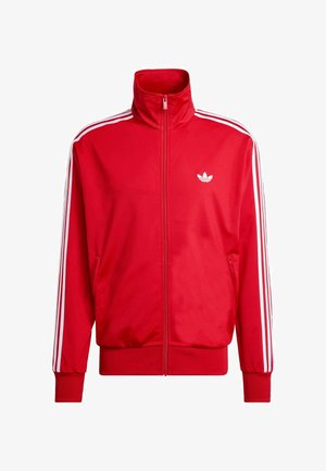 Jachetă de trening roșie cu fermoar, realizată dintr-un material neted, cu dungi albe pe mâneci și un mic logo alb pe piept.