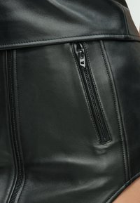 Μαύρο δερμάτινο σορτς με ορατή τσεπή με φερμουάρ στο πλάι, λεία υφή και ανθεκτική ραφή κατά μήκος των ραφών.